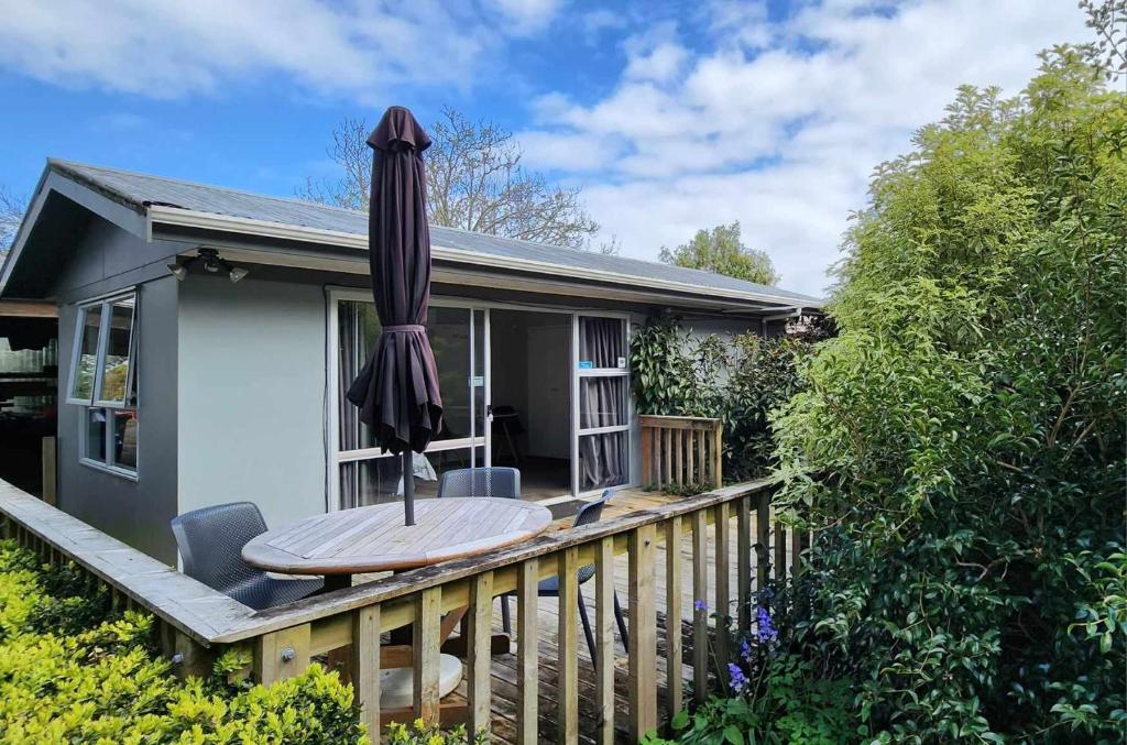a house with a table and an umbrella on a deck at Woodbury Farm B&B in Takanini
