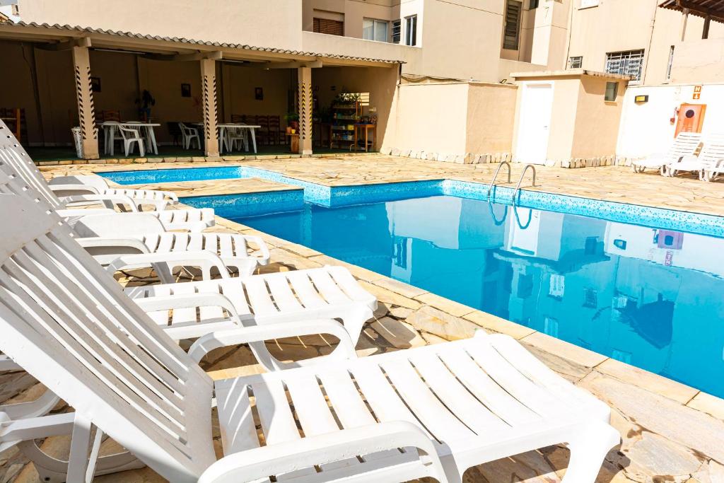 a group of white chairs sitting next to a swimming pool at Hotel Excelsior in Poços de Caldas