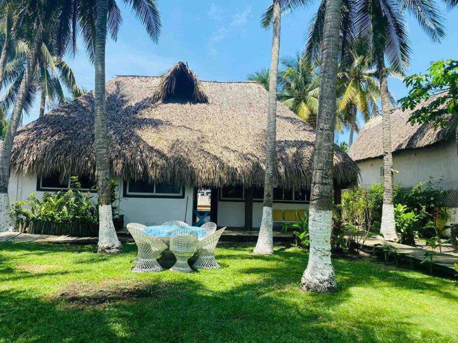 a house with a thatched roof with a table and palm trees at Casa de playa, en isla, frente al mar y canal in Iztapa