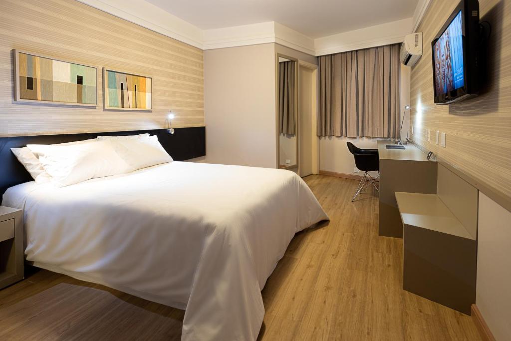 Habitación de hotel con cama blanca y TV en Momax Hotel, en Marília