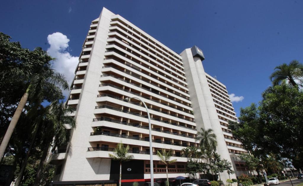 un grand bâtiment blanc avec des palmiers devant lui dans l'établissement Hotel Bonaparte Brasília - OZPED Flats, à Brasilia