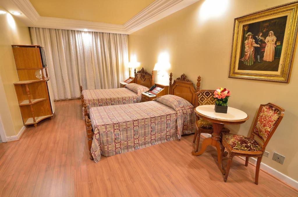 um quarto de hotel com duas camas e uma mesa e cadeira em Hotel Castelar em São Paulo