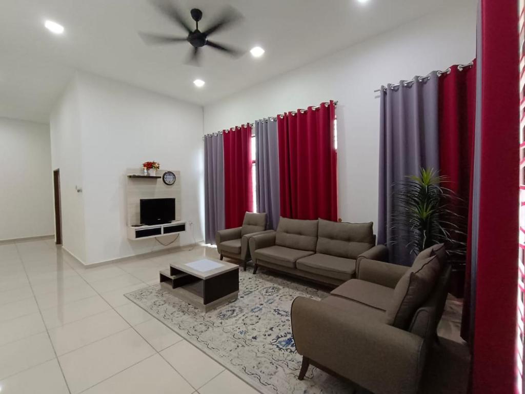 ein Wohnzimmer mit Sofas, einem TV und roten Vorhängen in der Unterkunft Homestay Gua Musang in Gua Musang