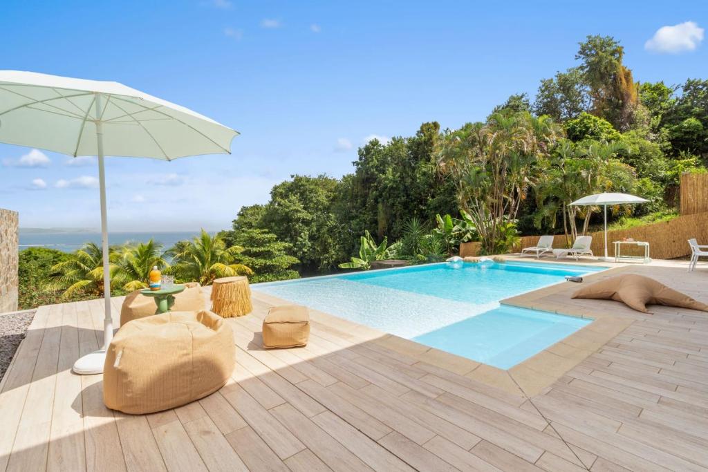 a swimming pool with an umbrella and chairs next to it at Villa Alexina in Le Robert