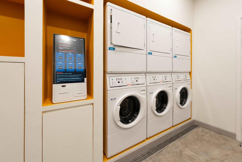 a laundry room with three washing machines and a tv at Wink Hotel Tuy Hoa Beach - 24hrs stay & Rooftop Pool Bar in Tuy Hoa