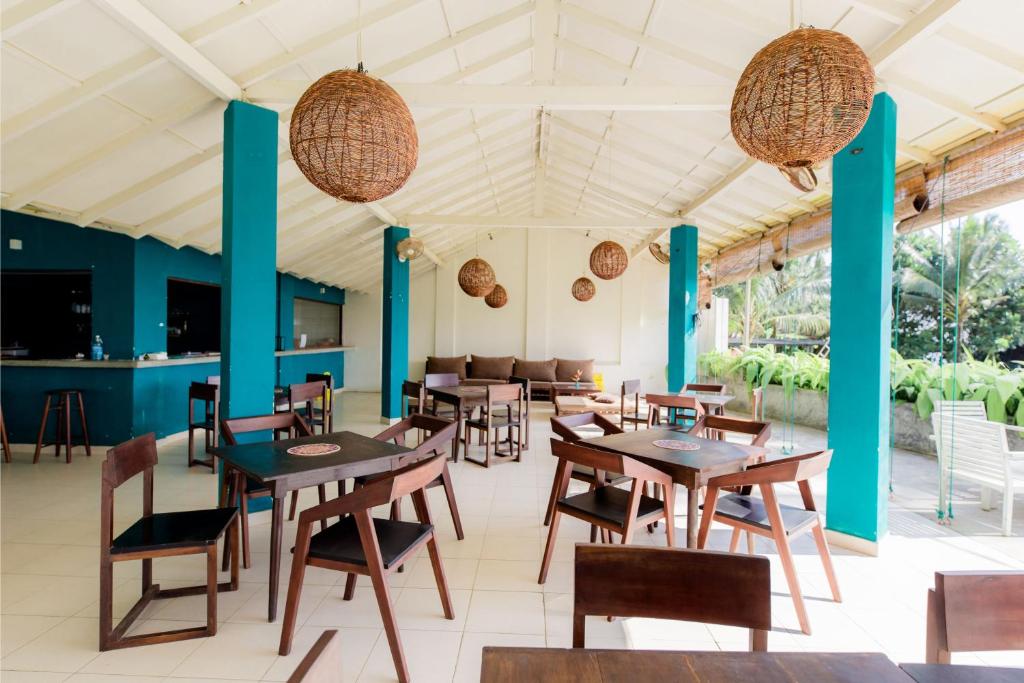 Shangrela Beach Resort by ARK في أمبالانغودا: مطعم بطاولات وكراسي خشبية وأعمدة زرقاء