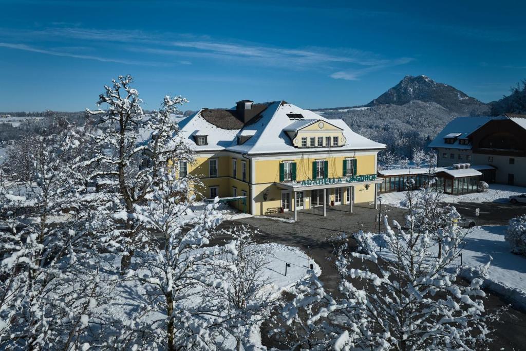 a large yellow house with a snow covered roof at Arabella Jagdhof Resort am Fuschlsee, a Tribute Portfolio Hotel in Hof bei Salzburg
