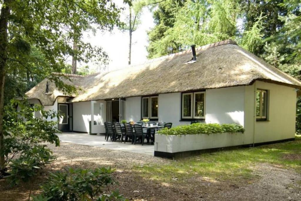 uma pequena casa branca com telhado de palha em Familiehuis de Lariks - 12 persoons villa op de Veluwe em Otterlo