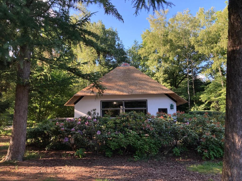 una pequeña casa con techo de paja y flores en Bungalow De Schuilevink - 8p MIVA, en Otterlo
