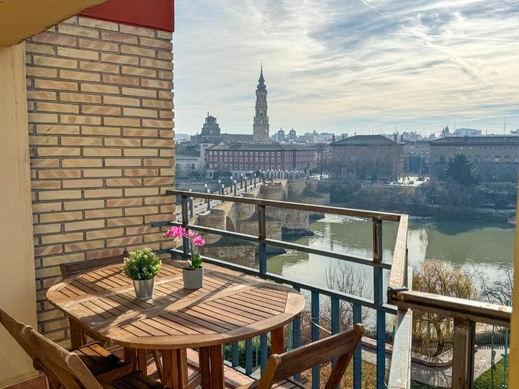 een balkon met een tafel en uitzicht op de rivier bij El Puente del Pilar ComoTuCasa in Zaragoza