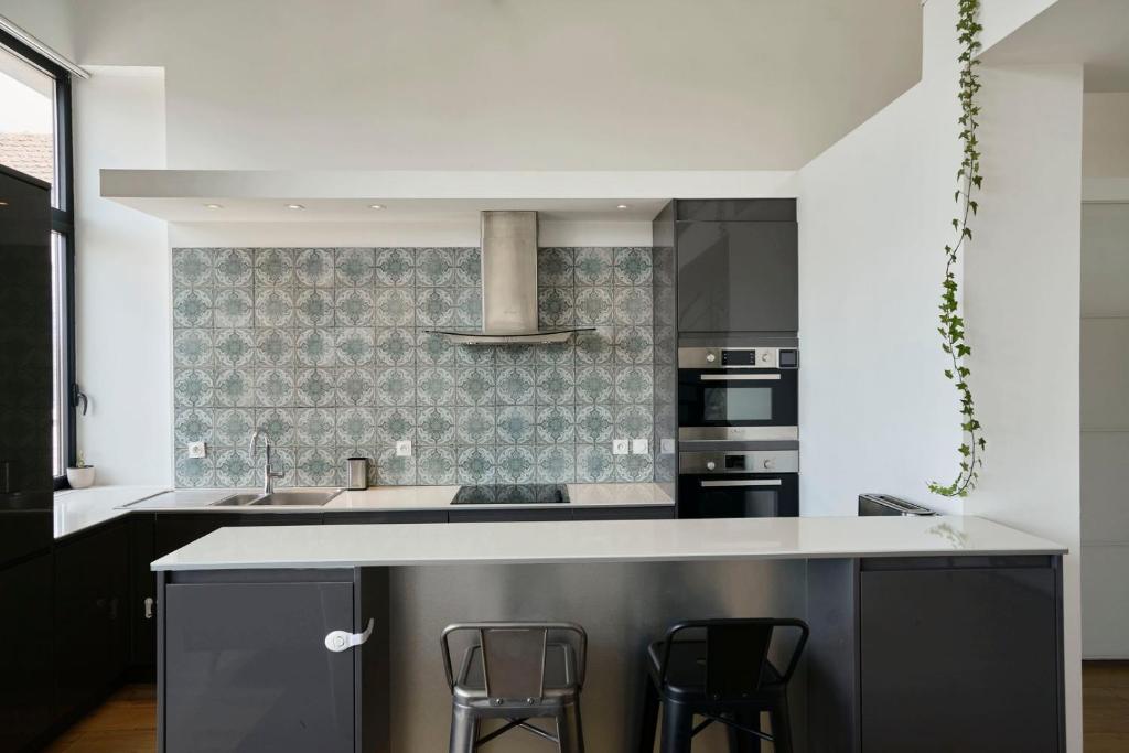 a kitchen with a counter and two stools in it at Loft en duplex atypique 4ch + parking in Tourcoing