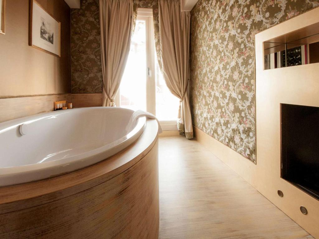 a large white tub in a bathroom with a window at Hotel Papadopoli Venezia - MGallery Collection in Venice