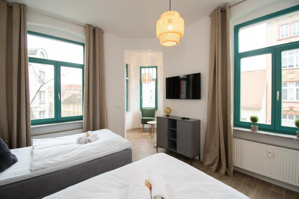 a bedroom with two beds and a tv and two windows at Room&Go: Zentral - Balkon - Arbeitsplatz in Halle an der Saale