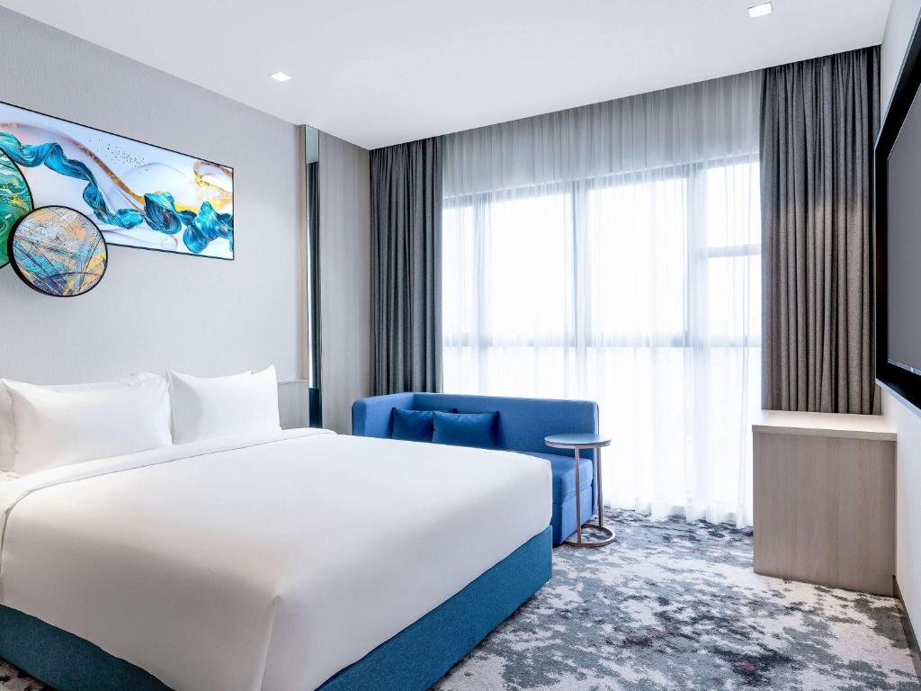 una camera con un letto bianco e una sedia blu di Mercure Kuala Lumpur Trion a Kuala Lumpur