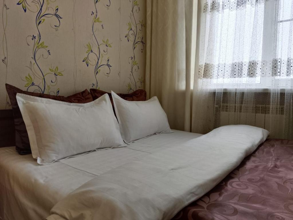 een bed met witte lakens en kussens in een slaapkamer bij Центр Гостеприимства in Aqtöbe