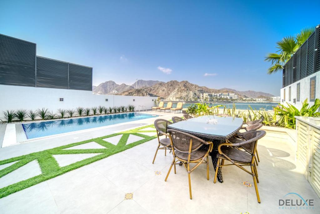 a patio with a table and chairs next to a pool at Grand 4BR Villa with Assistant's and Driver's Room Al Dana Island Fujairah by Deluxe Holiday Homes in Fujairah