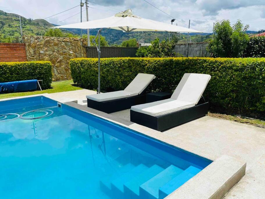 basen z 2 leżakami i parasolem w obiekcie Alegre villa con piscina para uso familiar de 3 dormitorios w mieście Paute