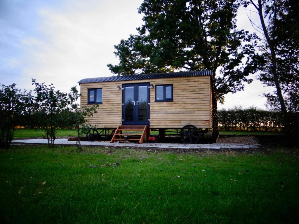 a tiny house sitting in a grassy field at The Dragonfly - Luxury Lakeside Shepherds Hut in Cotham
