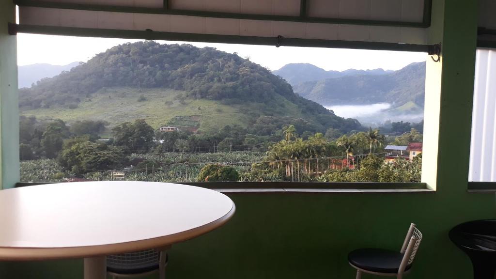 Itariri的住宿－Recanto de cachoeiras，一张桌子和椅子,在享有山景的窗户前
