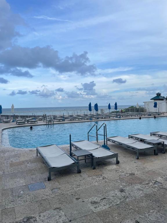 a swimming pool with picnic tables in front of the ocean at Marco Polo Beach Resort Condo with balcony in Sunny Isles Beach