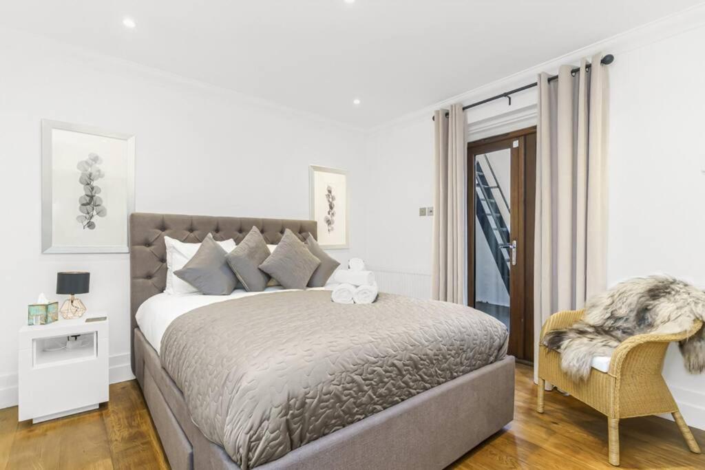 a white bedroom with a large bed and a chair at Notting Hill 2BR Gem l Stylish Prime Apt in London