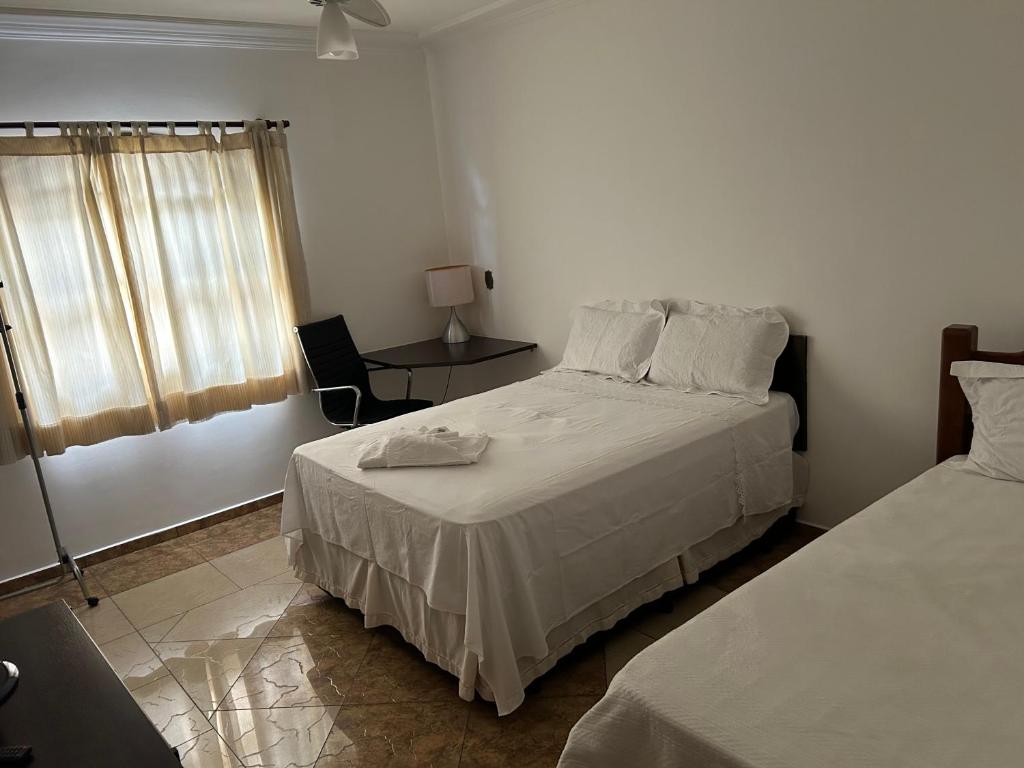 1 dormitorio con 2 camas, mesa y ventana en Quarto com / Bosque / Estoril / SJC, en São José dos Campos
