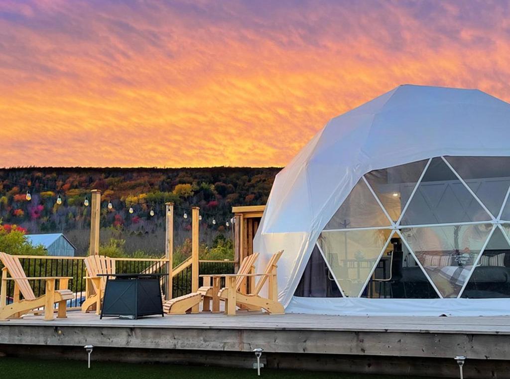 a tent with chairs on a deck with a sunset at Port Wade Glamping Domes in Victoria Beach 