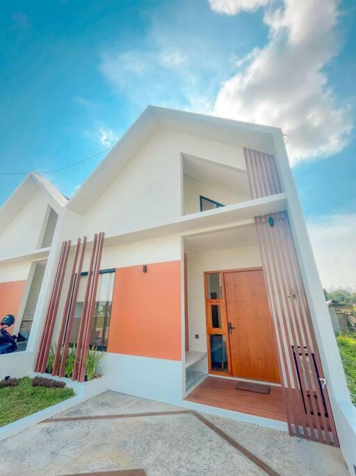 ein weißes Haus mit orangefarbener Tür vorne in der Unterkunft Villa Kamar Tamu Balecatur 2 in Sleman