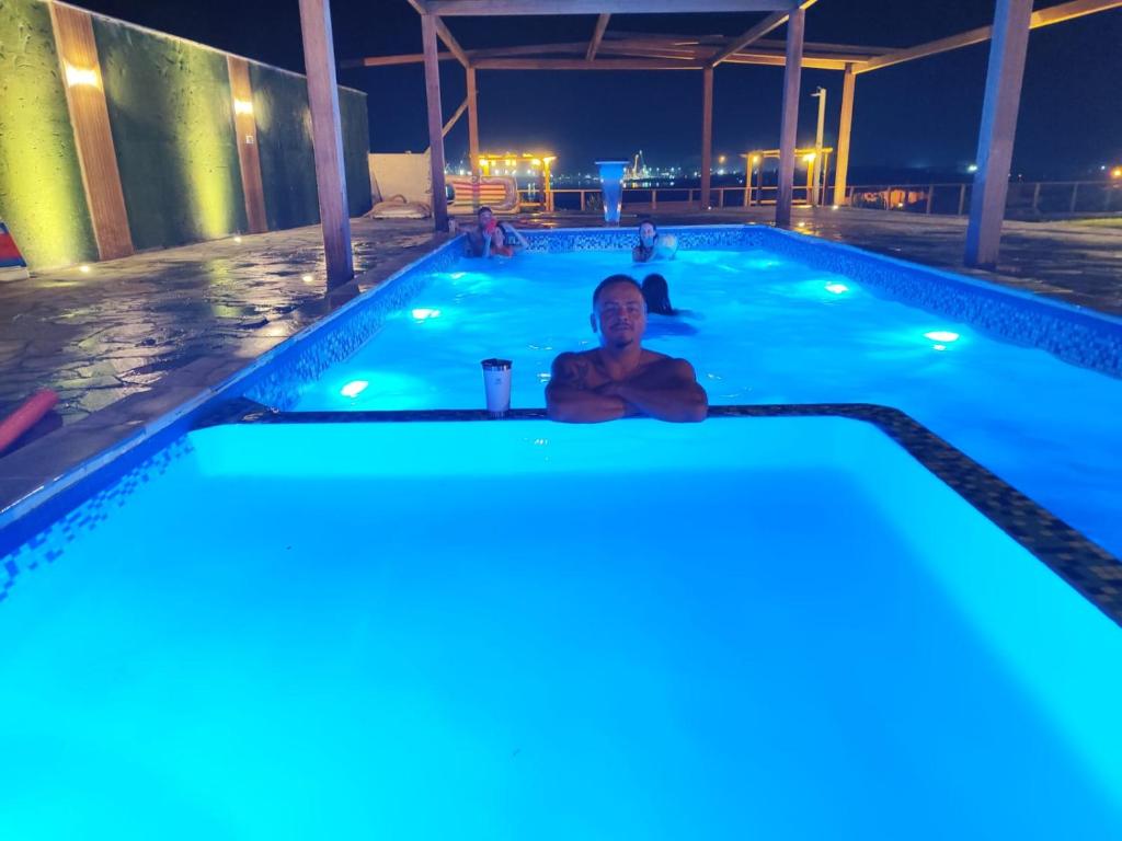 mężczyzna siedzący w basenie w nocy w obiekcie Chale vista do Porto Imbituba com piscina w mieście Imbituba