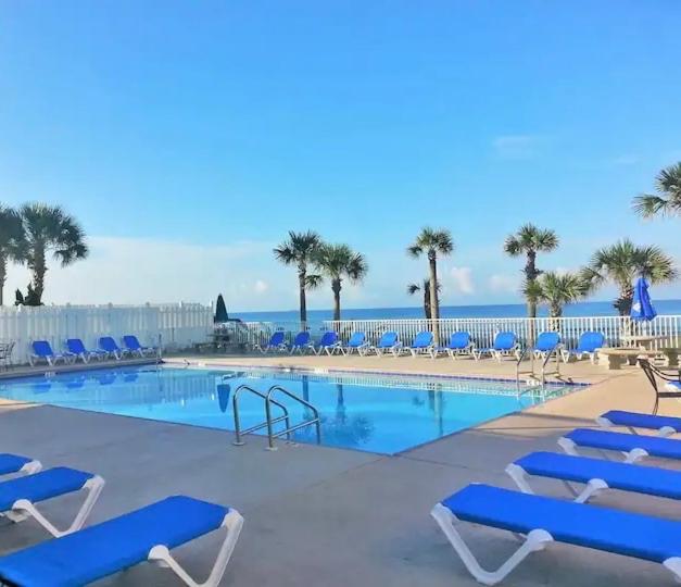 a swimming pool with blue chairs and the ocean at Sunny Daze, Desirable Kid Friendly Resort, 3 minute walk to the Beach, Resort Beachside Pool & Restaurant in Panama City Beach