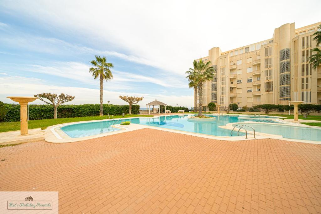 a large swimming pool with palm trees and a building at Cabo Mar Apartment sea view/pool in El Campello