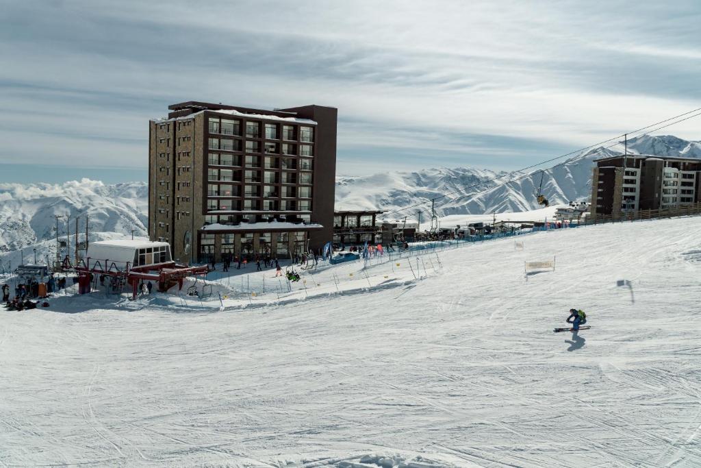 une personne skier sur une piste enneigée devant un bâtiment dans l'établissement Departamentos ALOJAMIENTO OFICIAL GRAN PARADOR ski in - out, Centro de Ski El Colorado, Farellones - Único con descuentos en servicios del Centro de Ski, à Farellones