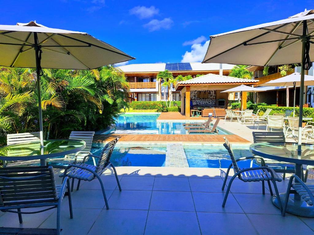 a patio with tables and chairs and a pool at Itacimirim - Village na Praia da Espera in Itacimirim