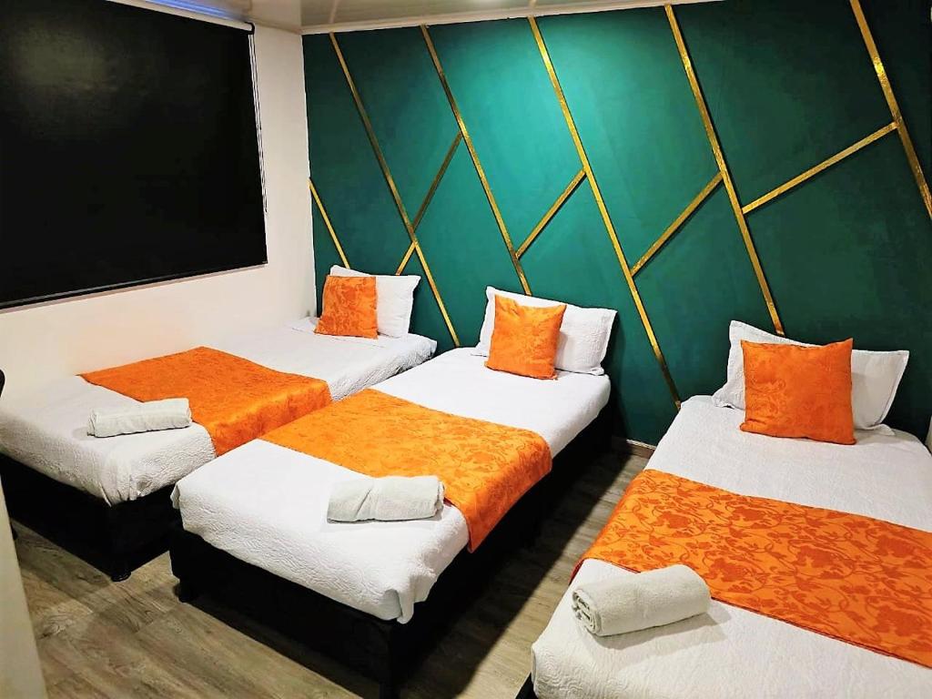 a room with three beds with orange and white sheets at Hotel Kristal Ferial in Bogotá