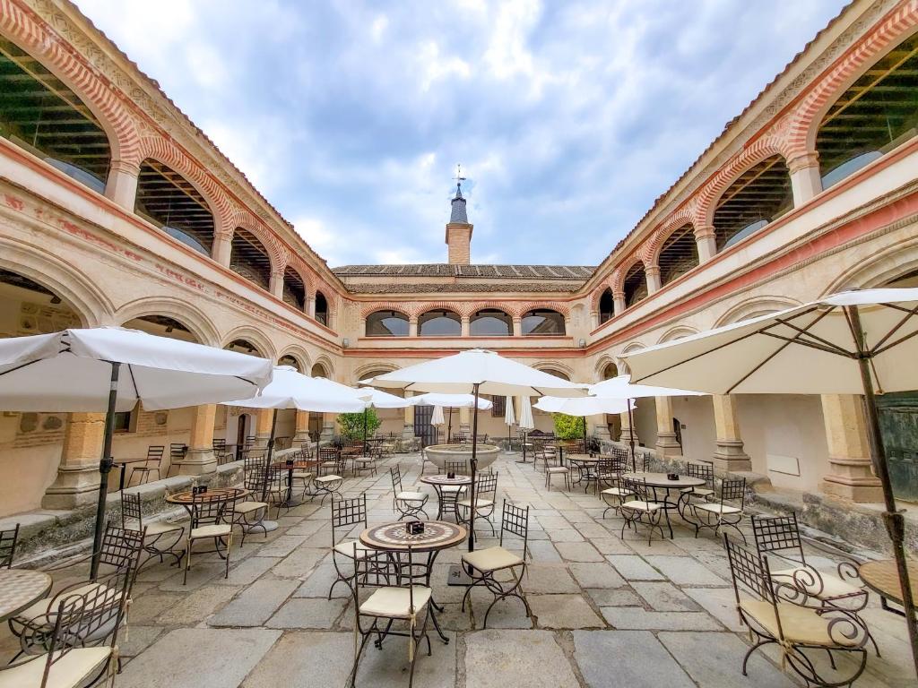 un patio vacío con mesas, sillas y sombrillas en Hotel San Antonio el Real, en Segovia