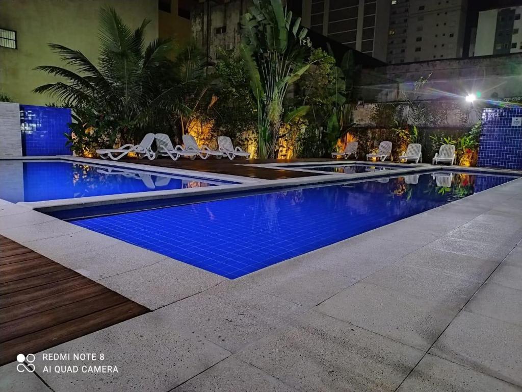 a swimming pool at night with lounge chairs around it at Flat Pitangueira com Piscina-Capitânia Varan in Guarujá