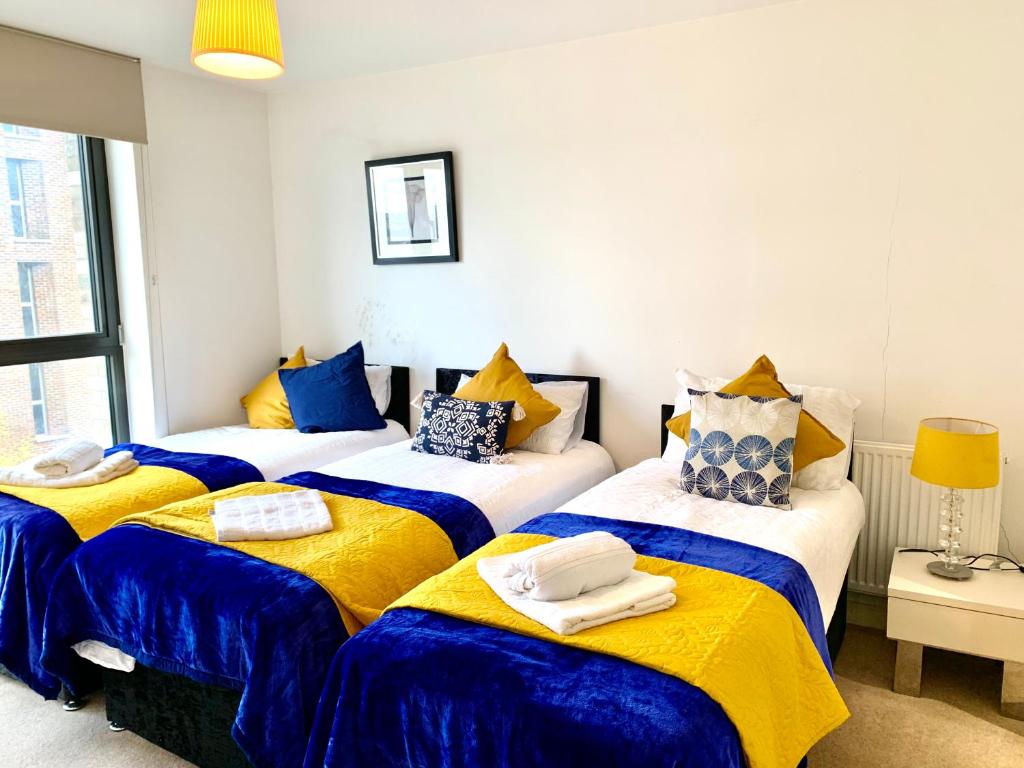 three beds in a room with blue and yellow sheets at Modern London Excel 2 Bedrooms 2 Bathrooms, Parking, Kitchen, Lounge, Balcony Apartment in London