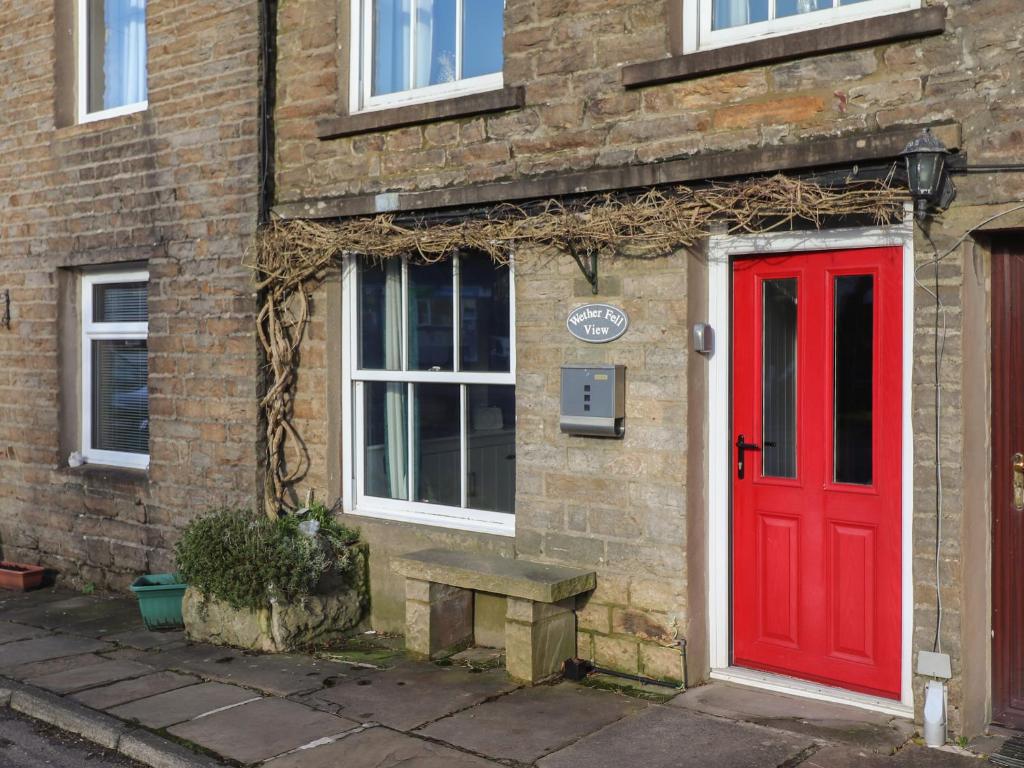 a red door and a bench in front of a brick building at Wether Fell View in Hawes