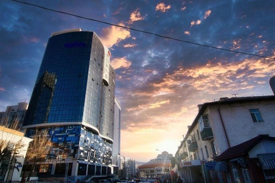 un alto edificio di vetro su una strada di città al tramonto di Tokyo Business Apartment a Ulaanbaatar
