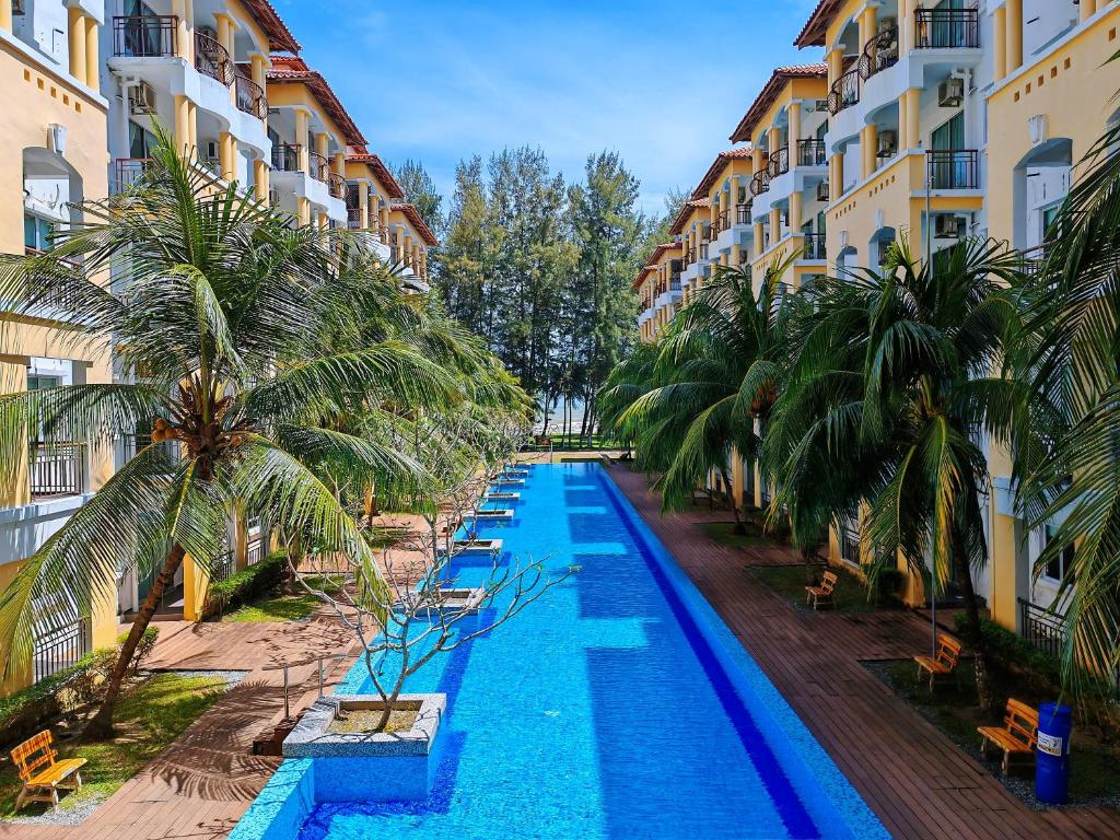 a swimming pool in front of a building with palm trees at Desaru Black Beach Sky Mirror Resort in Desaru