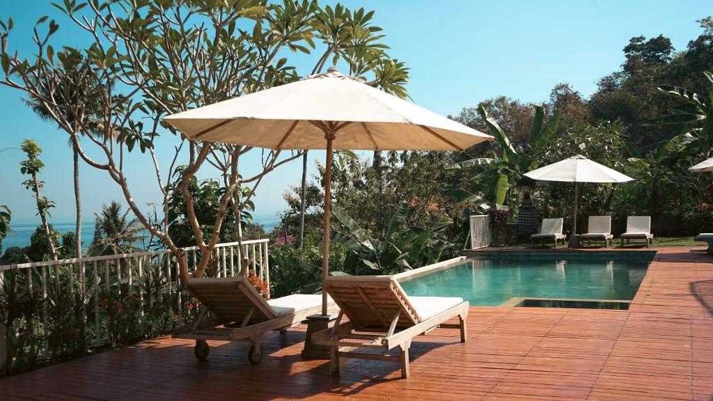 a patio with two chairs and an umbrella next to a pool at La Gautch Bungalow in Nusa Lembongan