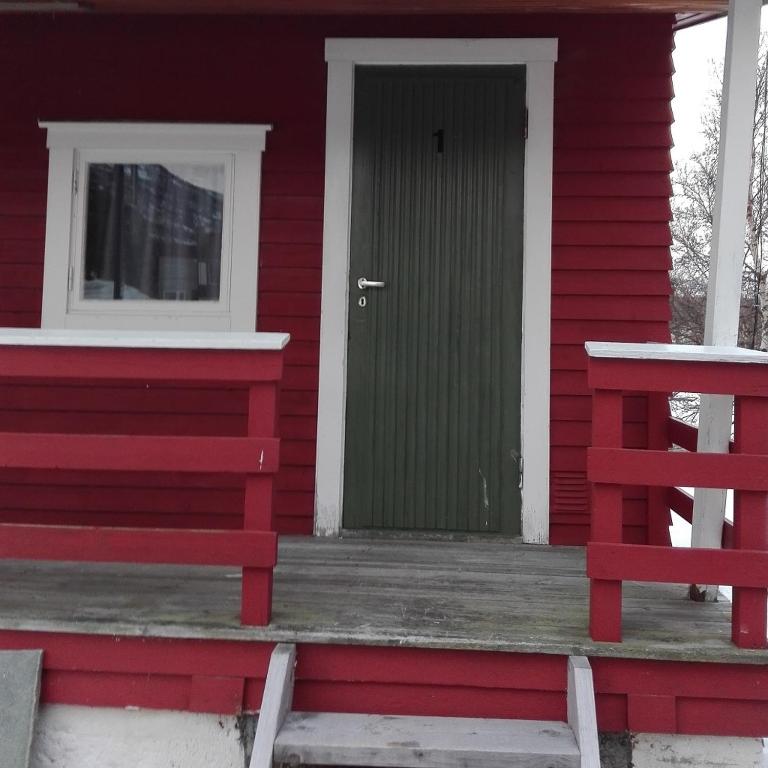 una casa roja con una puerta verde y un banco en ekspressen-camping, en Manndalen