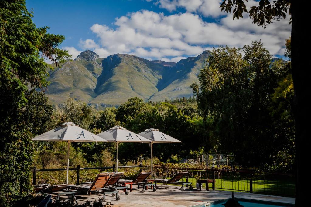 a patio with chairs and umbrellas with mountains in the background at Aan de Oever Guesthouse in Swellendam