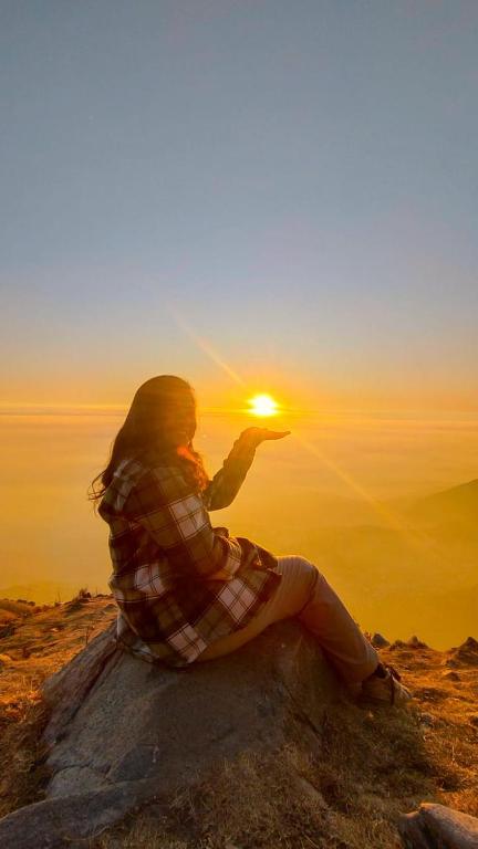 a woman sitting on a rock looking at the sunset at Triund Trek in Dharamshala