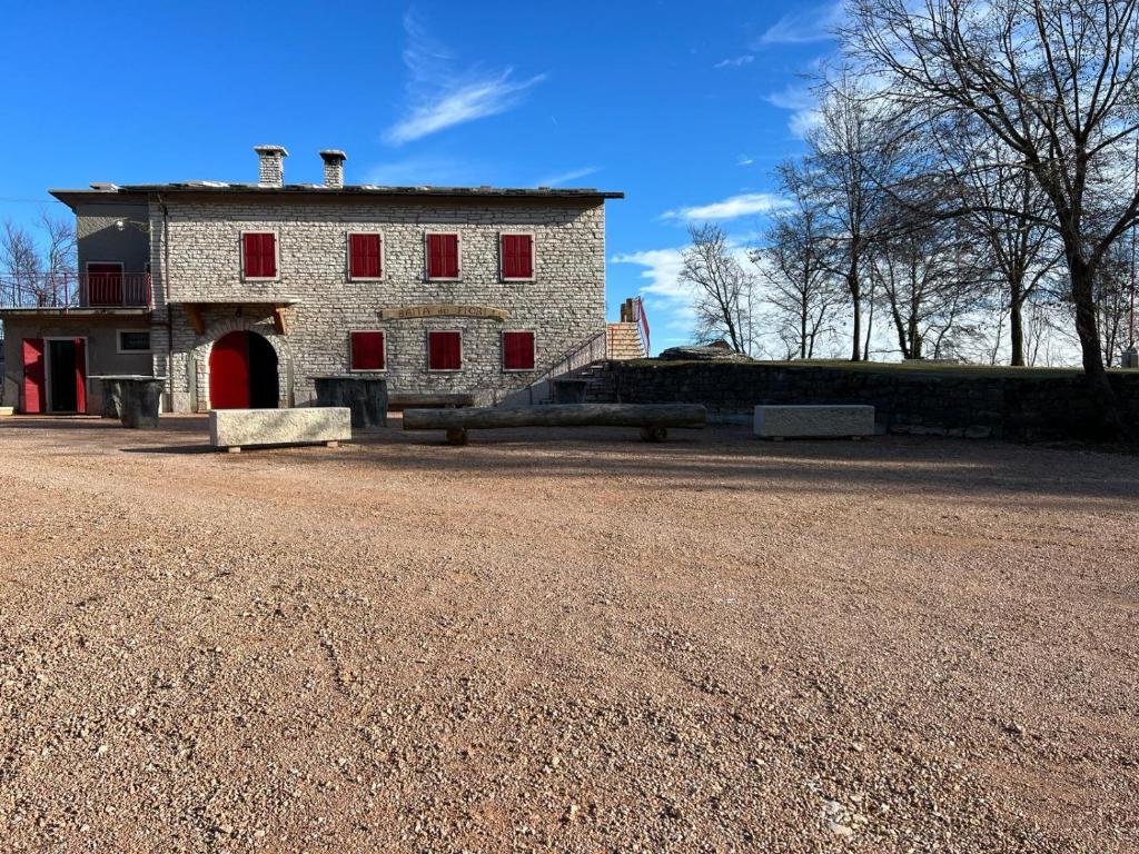 un vieux bâtiment avec des fenêtres rouges sur un chemin de terre dans l'établissement VALPOCENTER - Baita dei Fiori, à SantʼAnna dʼAlfaedo