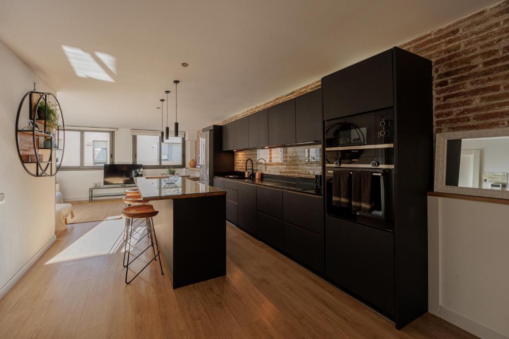 a kitchen with black cabinets and a brick wall at Atico duplex Playa Area barcelona con SPA exterior in Montgat