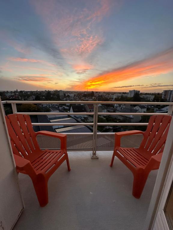 zwei rote Stühle auf einem Balkon mit Sonnenuntergang in der Unterkunft Appartement NEUF et cosy à Blois in Blois