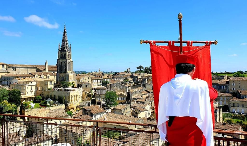 a man in a cape standing on a roof looking at a city at La maison d artiste in Saint-Émilion