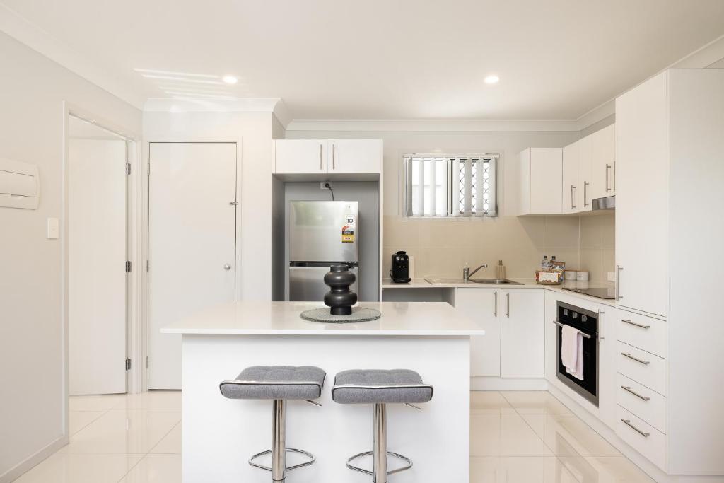a kitchen with white cabinets and a counter with two stools at Aircon! Parking! Host with 100s of 5 star reviews! in Brisbane