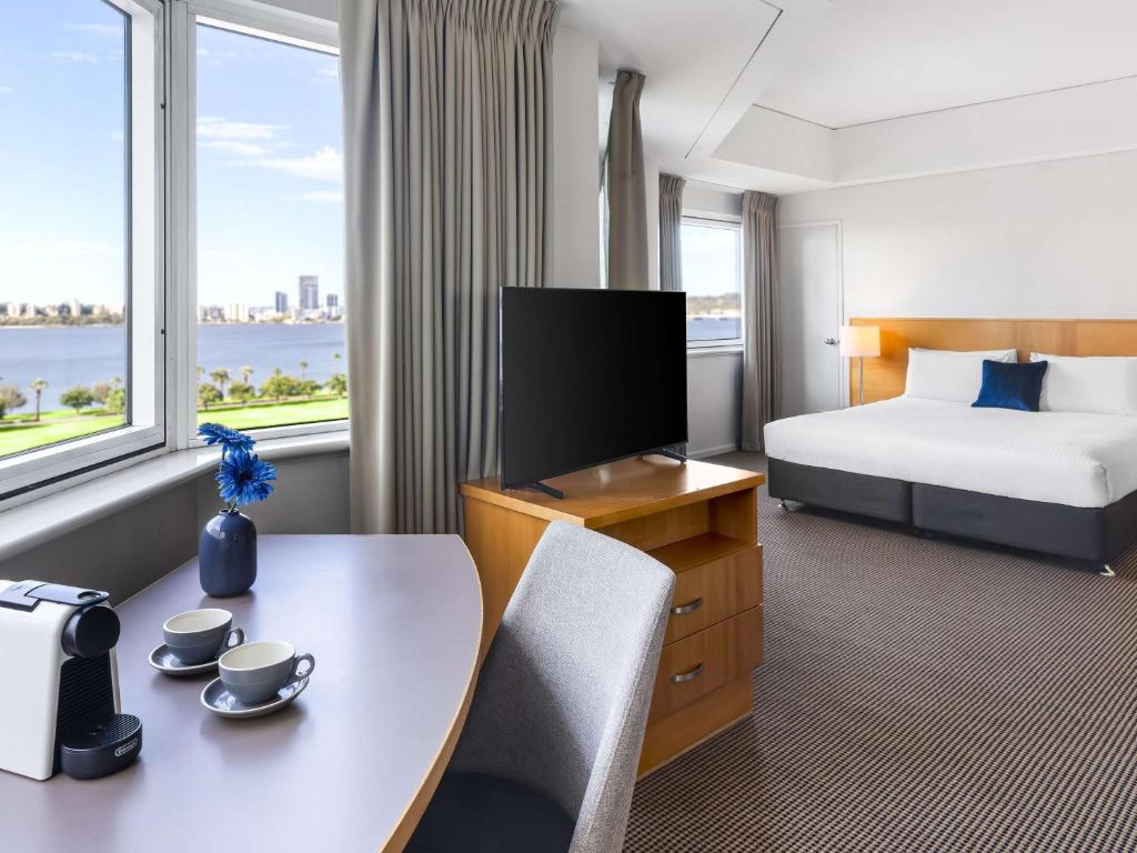 a hotel room with a bed and a desk with a table at Novotel Perth Langley in Perth